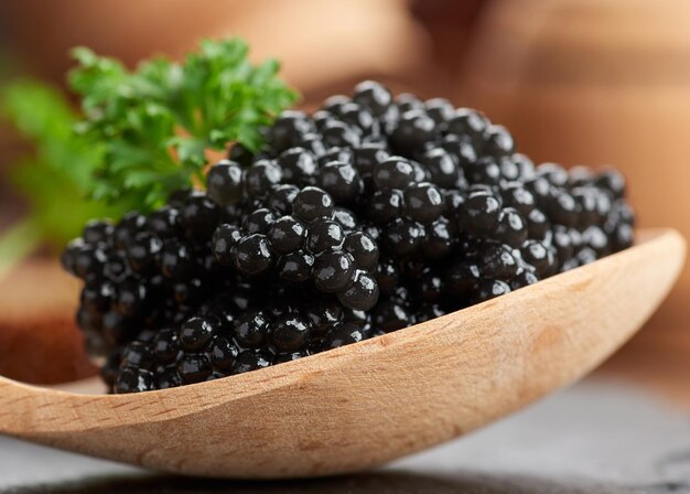 Caviar de pez espátula negro granulado fresco en cuchara de madera marrón sobre un fondo negro, cerrar