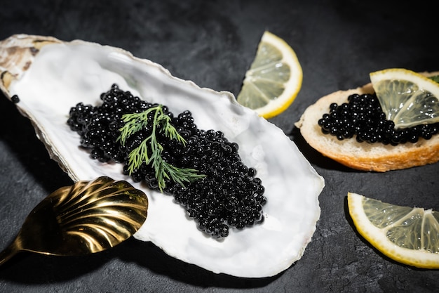 Caviar preto com rodelas de limão em uma mesa de madeira preta. A colher de ouro está próxima. Deliciosas iguarias. Comida rica. Fechar-se.