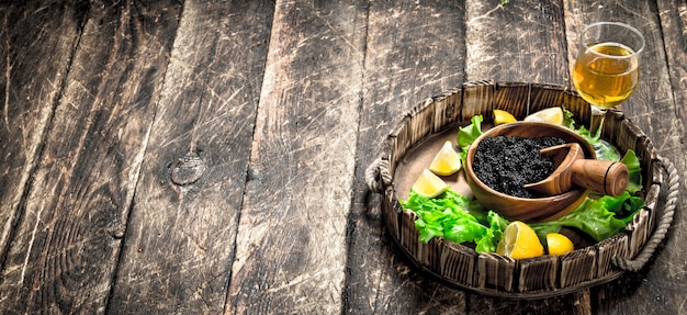 Caviar preto com uma taça de vinho e verduras na mesa de madeira.