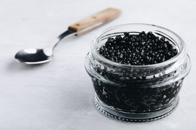 Caviar preto em frasco de vidro sobre fundo de pedra branca, guloseima luxuosa, espaço de cópia de aperitivo