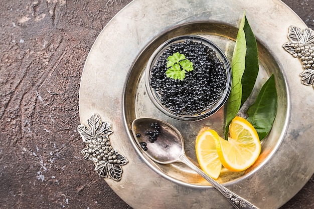 Caviar preto em uma tigela de vidro com limão, close-up sobre a vista superior da superfície escura