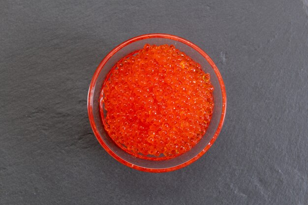 Caviar rojo en el frasco de vidrio en el boardound de piedra gris