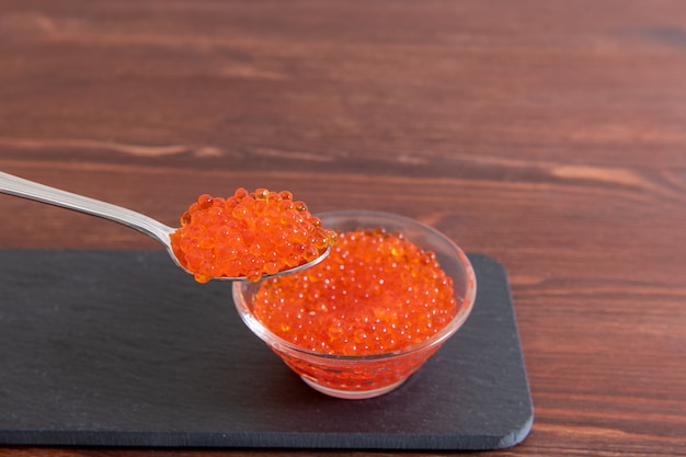 Caviar rojo en frasco de vidrio con cuchara de plata en la madera marrón oscura