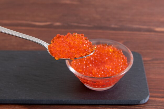 Caviar rojo en frasco de vidrio con cuchara de plata en la madera marrón oscura