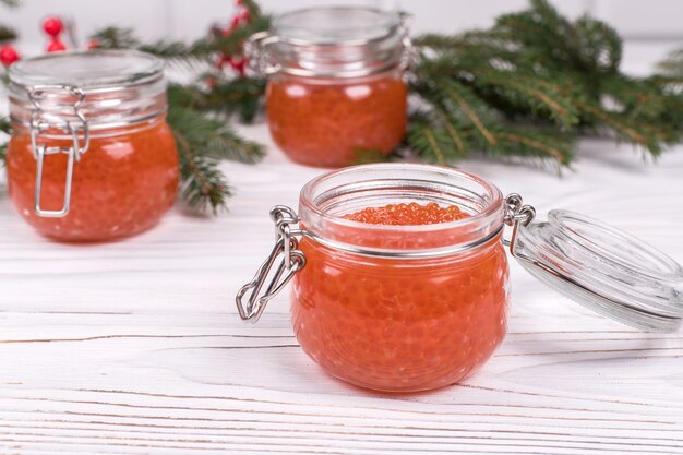 Caviar rojo en frasco de vidrio sobre fondo de madera blanca envejecida. Plato principal Año Nuevo.