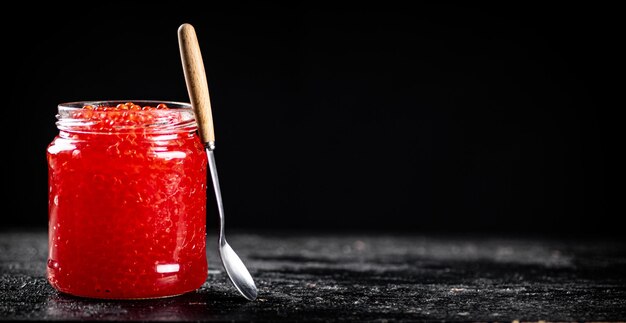 Caviar rojo en un frasco de vidrio sobre una mesa con una cuchara