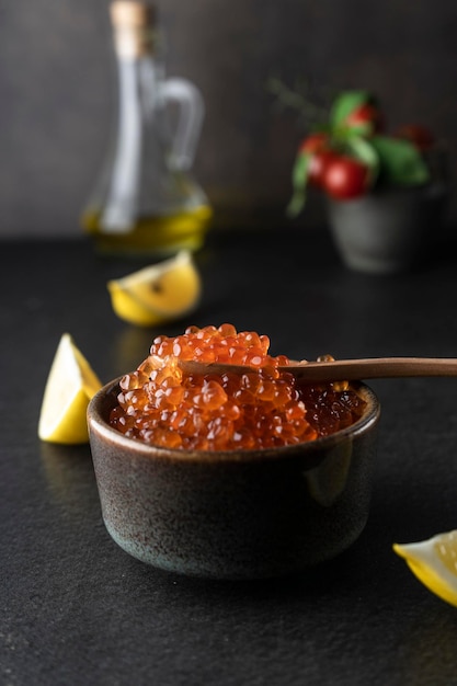 Caviar rojo fresco con una cuchara de madera sobre un fondo oscuro en un recipiente de cerámica copyspace