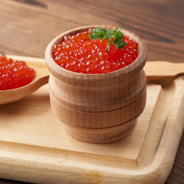 Caviar rojo granulado en un recipiente de madera sobre una mesa marrón