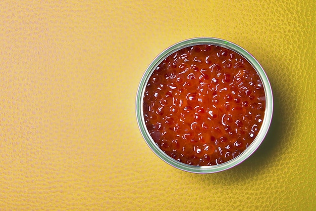 Caviar rojo en la lata abierta sobre un fondo amarillo