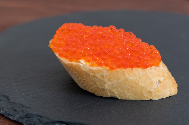 Caviar rojo con pan blanco sobre la piedra gris boardound