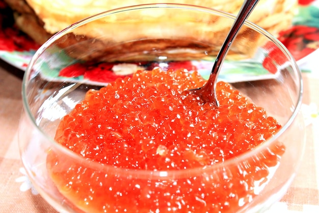 Caviar rojo en un plato con la cuchara y panqueques en el fondo