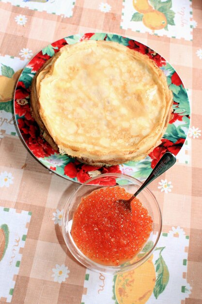 Caviar rojo en un plato con la cuchara y panqueques en el fondo