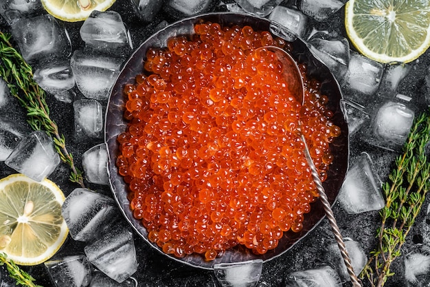 Caviar rojo salado en placa de acero sobre hielo Fondo negro Vista superior