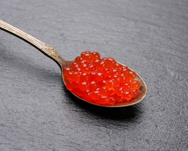 Caviar rojo de salmón chum en una cuchara de metal sobre un fondo negro, cerrar