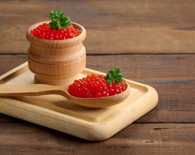 Caviar rojo de salmón rosado se encuentra en una cuchara de madera sobre una tabla de cortar Mesa de madera marrón