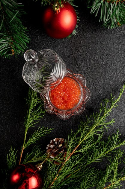 Caviar rojo sobre un fondo oscuro de Navidad decorado con juguetes y ramas