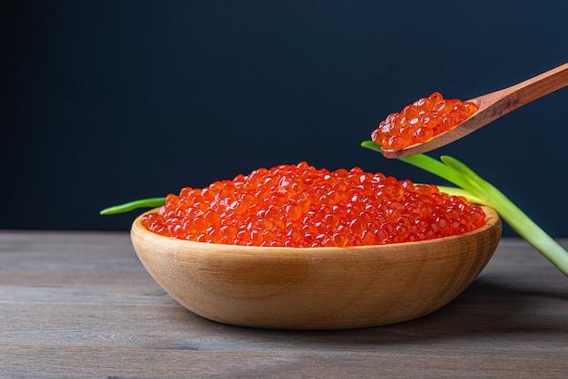 Caviar rojo en una taza de madera sobre un fondo de madera con una cuchara. Lugar para publicidad, logotipo, etiqueta, maqueta, maqueta.