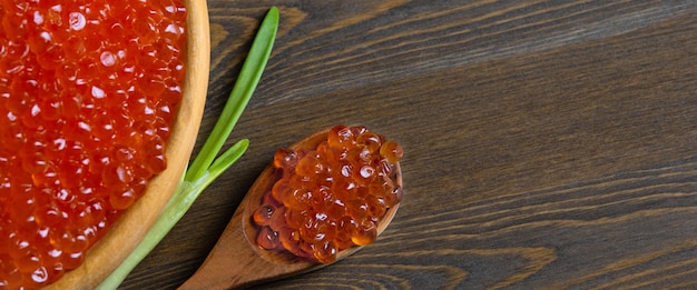 Caviar rojo en una taza de madera sobre un fondo de madera con una cuchara.