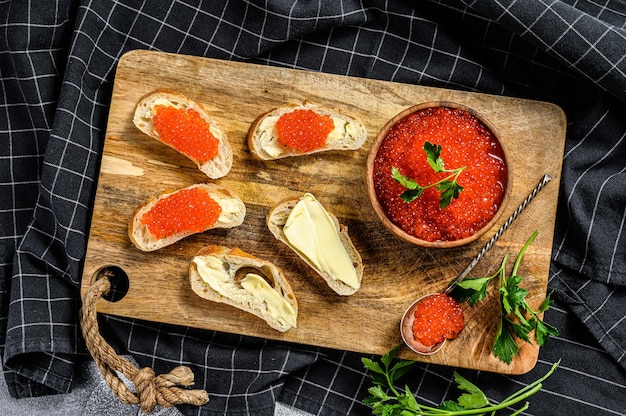 Caviar rojo en tazón de madera y sándwiches en tabla de cortar