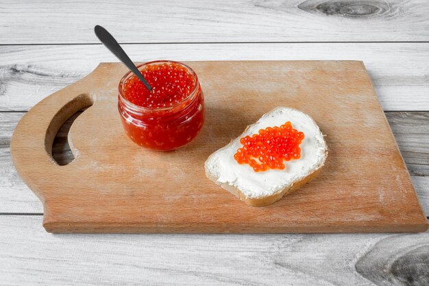 Caviar de salmón rojo en un frasco y en un sándwich de mantequilla.