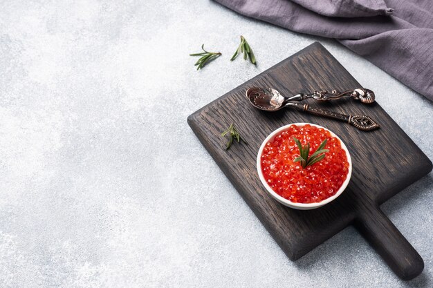 Caviar de salmón rojo en un plato sobre una tabla para cortar madera.