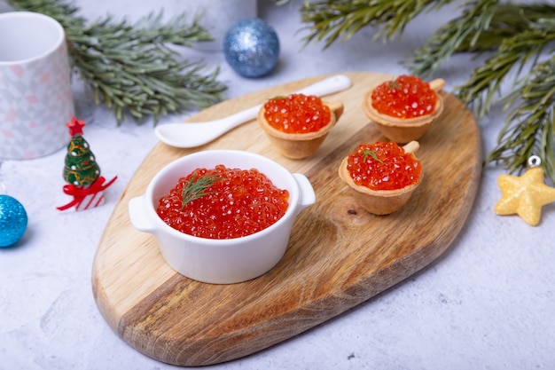 Caviar vermelho (caviar de salmão) em uma tigela branca em uma placa de madeira