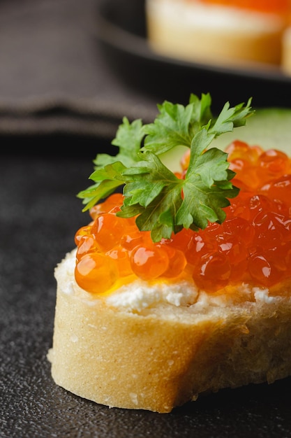 Caviar vermelho com salsa no pão Canapé em fundo preto Delicadeza de salmão de luxo Vista lateral aproximada