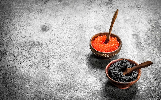 Caviar vermelho e preto em tigelas de madeira. Sobre fundo rústico.