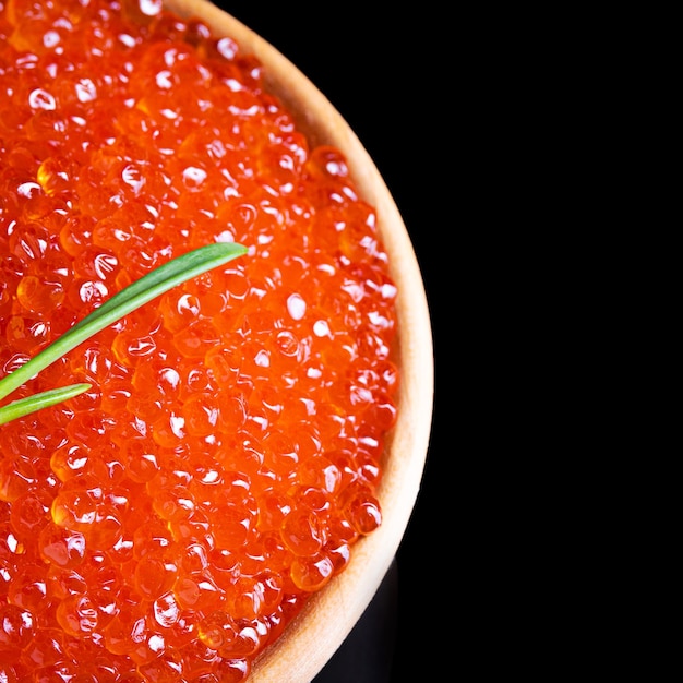 Caviar vermelho em um copo branco em um fundo preto