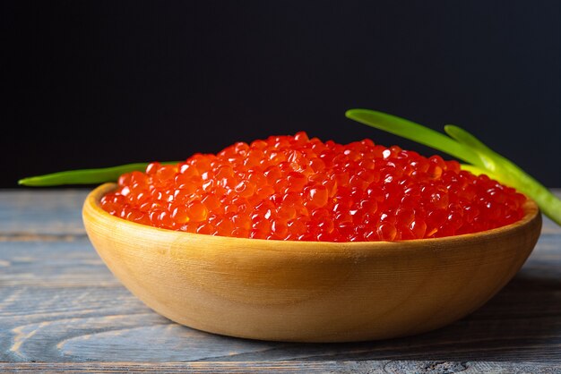 Caviar vermelho em um copo de madeira com fundo de madeira.