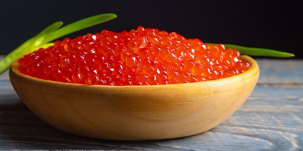 Caviar vermelho em um copo de madeira com fundo de madeira.