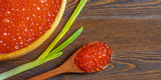 Caviar vermelho em um copo de madeira em um fundo de madeira com uma colher.