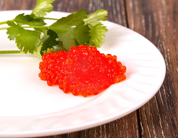 Caviar vermelho em um prato branco com ervas na madeira