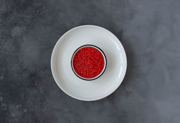 Caviar vermelho em um prato branco sobre um fundo escuro. vista do topo. copie o espaço