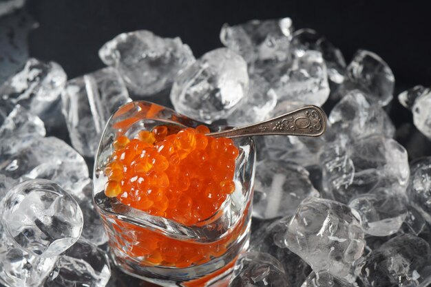 Caviar vermelho em uma colher no fundo do gelo. Caviar de salmão de close-up. Delicatessen