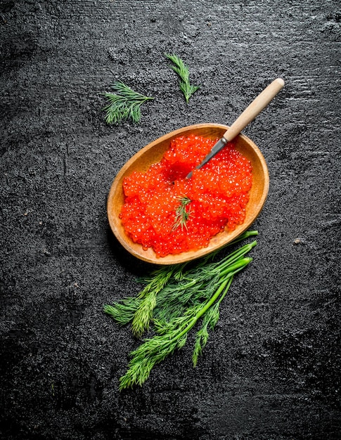 Caviar vermelho em uma tigela com uma colher e endro