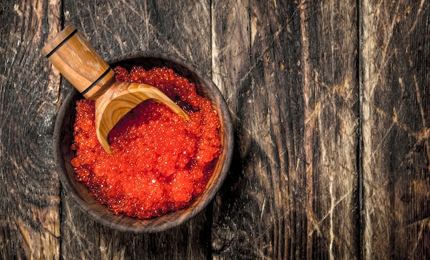 Caviar vermelho em uma tigela com uma pá. Em fundo de madeira.