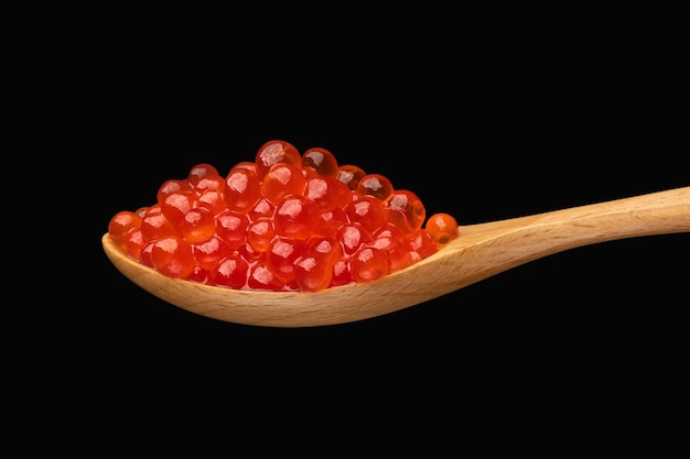 Foto caviar vermelho exclusivo na colher de pau isolada em fundo escuro