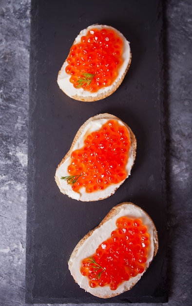 Caviar vermelho fresco no pão na chapa preta. Sanduíches com caviar vermelho. Delicatessen. Comida gourmet.