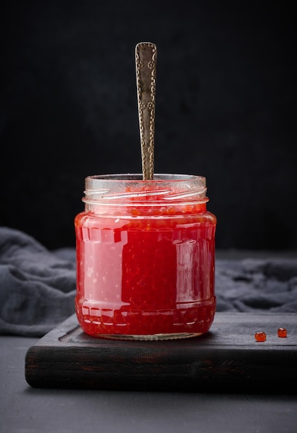 Caviar vermelho granulado fresco em uma jarra de vidro em uma mesa de madeira