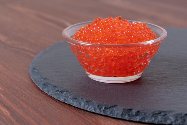 Caviar vermelho na jarra de vidro na mesa de madeira marrom escura