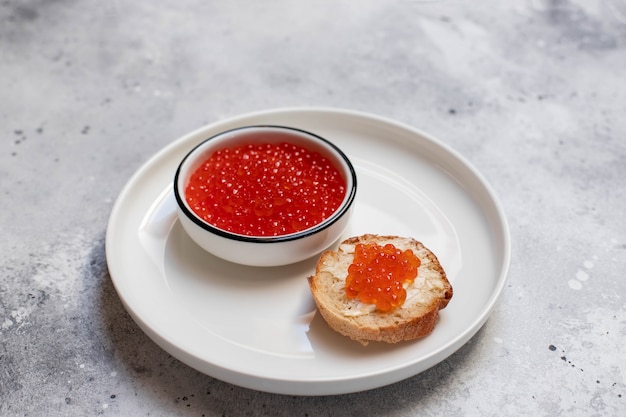 Caviar vermelho salmão em um prato branco sobre um fundo claro. frutos do mar. lanche