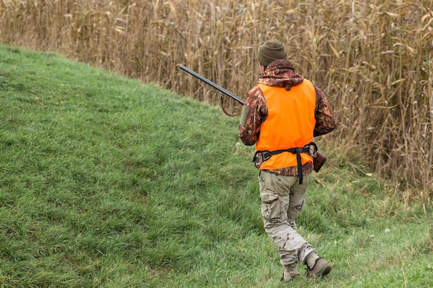 Un cazador con un arma en sus manos en ropa de caza en el bosque de otoño en busca de un trofeo Un hombre está parado con armas y perros de caza rastreando el juego