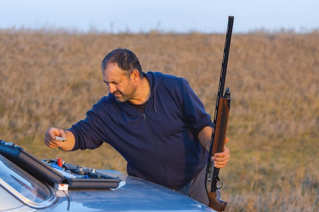 Un cazador con un arma en sus manos en ropa de caza en el bosque de otoño en busca de un trofeo Un hombre está parado con armas y perros de caza rastreando el juego