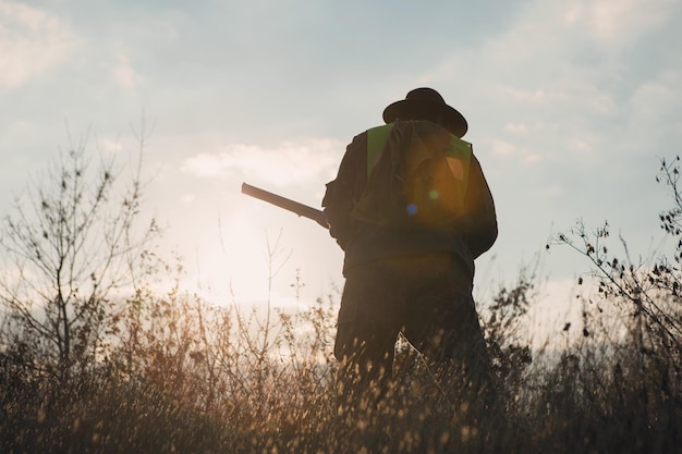 Un cazador con un arma en sus manos en ropa de caza en el bosque de otoño en busca de un trofeo Un hombre está parado con armas y perros de caza rastreando el juego