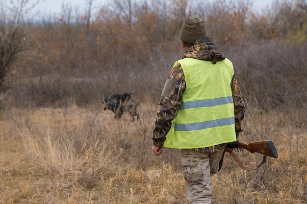 Un cazador con un arma en sus manos en ropa de caza en el bosque de otoño en busca de un trofeo Un hombre está parado con armas y perros de caza rastreando el juego