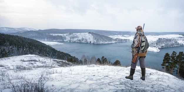 Cazador en camuflaje con escopeta en la vista panorámica de caza de invierno con espacio de copia