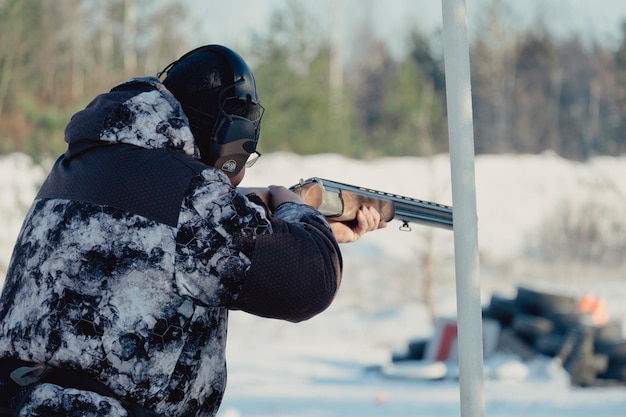 Cazador de camuflaje con rifle en bosque de invierno. Concepto de caza. Hombre asegurando una reserva, en un día de nieve. Hunter apunta con un arma en el bosque nevado