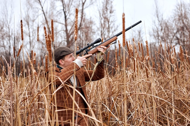 El cazador caucásico europeo está cazando en el bosque mirando a través del enfoque suave del rifle en el campo m