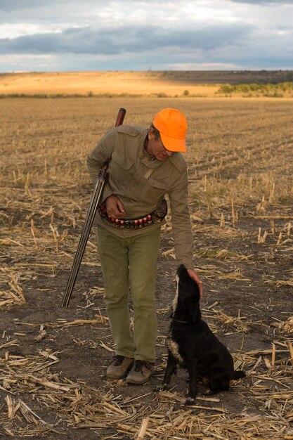 Cazador de faisanes con un arma y perros en el contexto de una espectacular puesta de sol